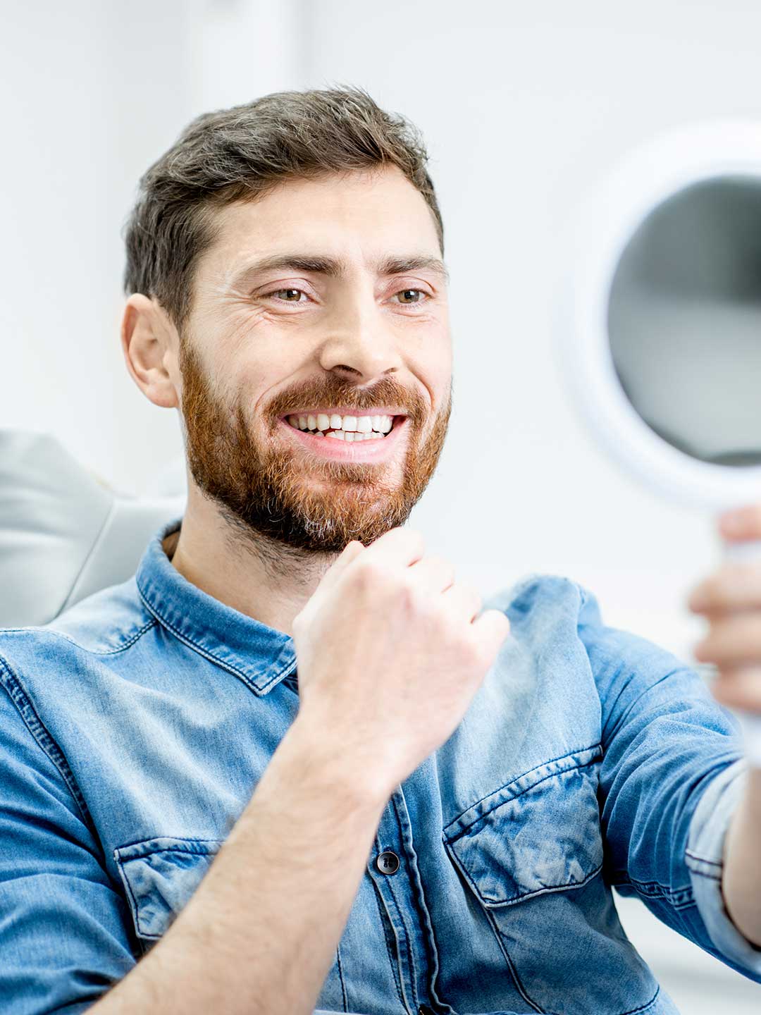 Happy male patient checking his smile after cosmetic gum treatment at Harmony Medical Center.