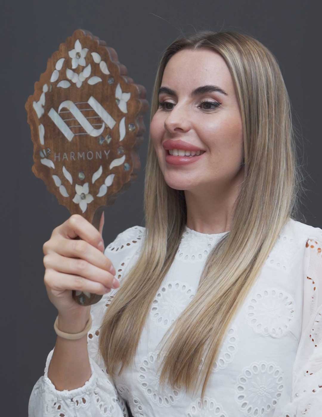 Beautiful woman checks her new smile in the mirror after a full mouth rehabilitation at Harmony Medical Center.